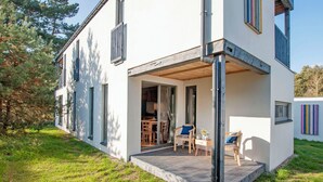 Une maison moderne à deux étages, dotée d’un porche couvert, d’un coin repas et dont l’intérieur est visible à travers les portes vitrées.