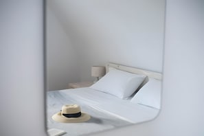 A bed with white linens, a nightstand with a lamp, and a straw hat on the bed.