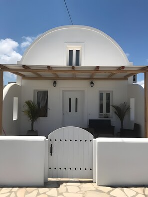 A white building with a dome roof, a wooden pergola, a white gate, and potted plants.