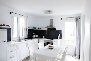 A modern kitchen with white cabinetry, a black stove, and a dining area with a white table and chairs.