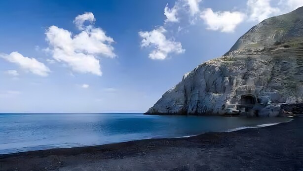 A coastal landscape with a rocky cliff, a beach, and a clear sky.