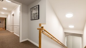 A hallway with a wooden handrail, a framed artwork on the wall, and recessed ceiling lights.