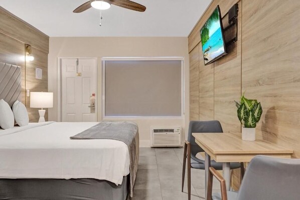 Habitación de hotel con cama, mesita de noche, lámpara, televisor y una pequeña mesa con sillas.