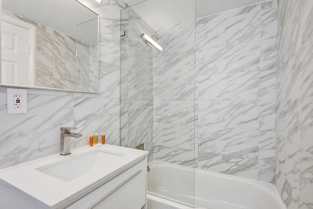 A bathroom with a marble wall, a sink, a mirror, a shower, and a bathtub.
