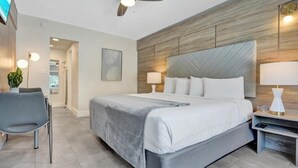 Ein modernes Hotelzimmer mit einem großen Bett, einem Schreibtisch, einem Sessel, einem Deckenventilator und einem Nachttisch mit Lampe.