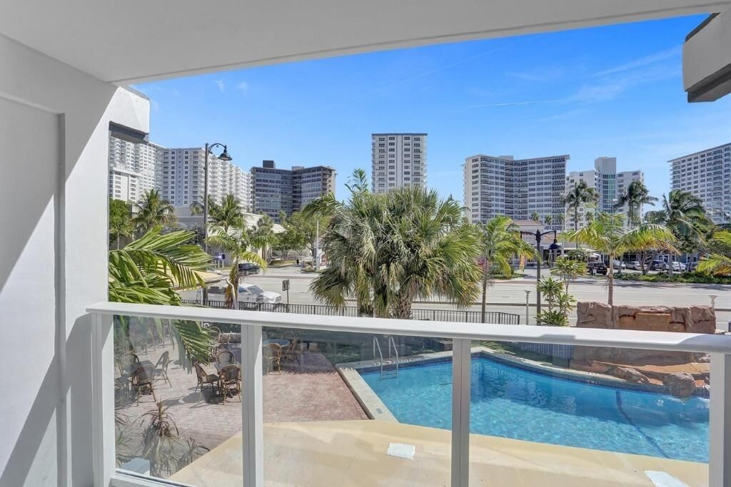 Ein Balkon mit Blick auf einen Swimmingpool, Palmen und hohe Gebäude im Hintergrund.