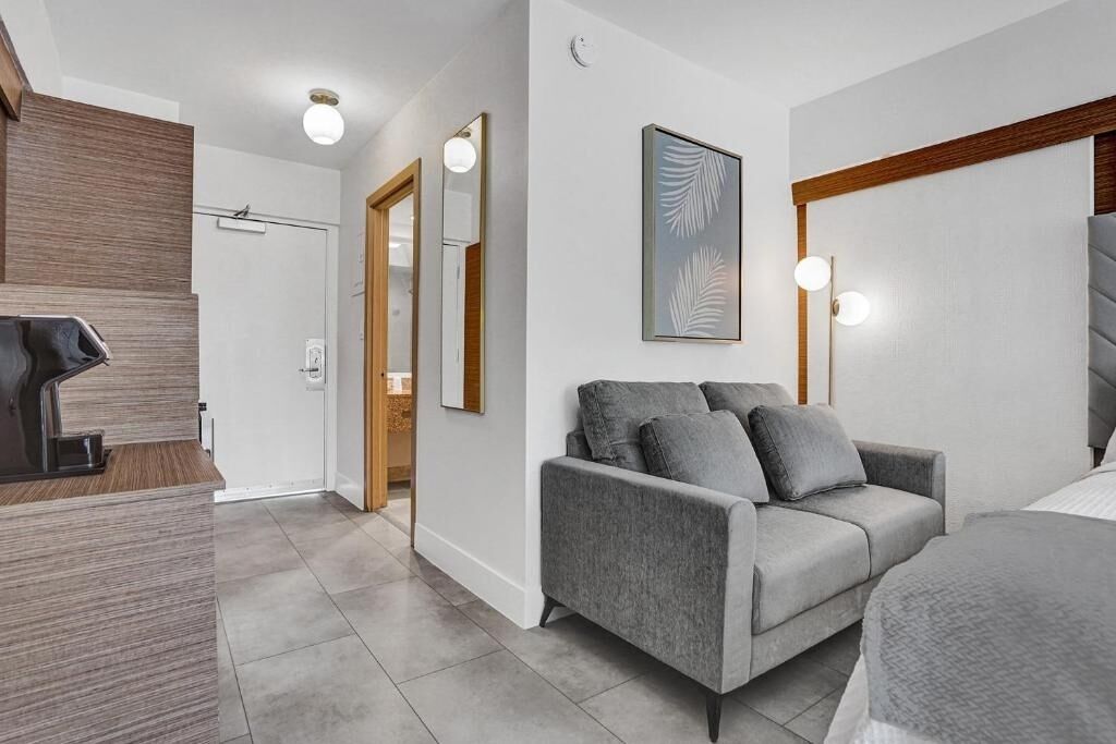 Ein modernes Hotelzimmer mit grauem Sofa, einem Bett, einem Holztisch und einem großen Spiegel.