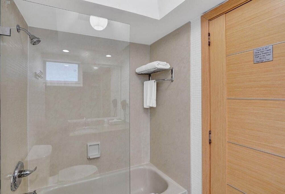 Une salle de bain moderne avec une douche à parois de verre, une baignoire blanche et une porte en bois.