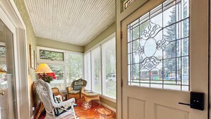 A sunroom with a rocking chair, a small table, and a decorative window.
