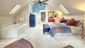 A bedroom with a large bed, a ceiling fan, a bathtub, and a walk-in closet.