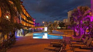 Zona de piscina de hotel con sillones de descanso, palmeras y un letrero que indica el Hotel Royal Beach.