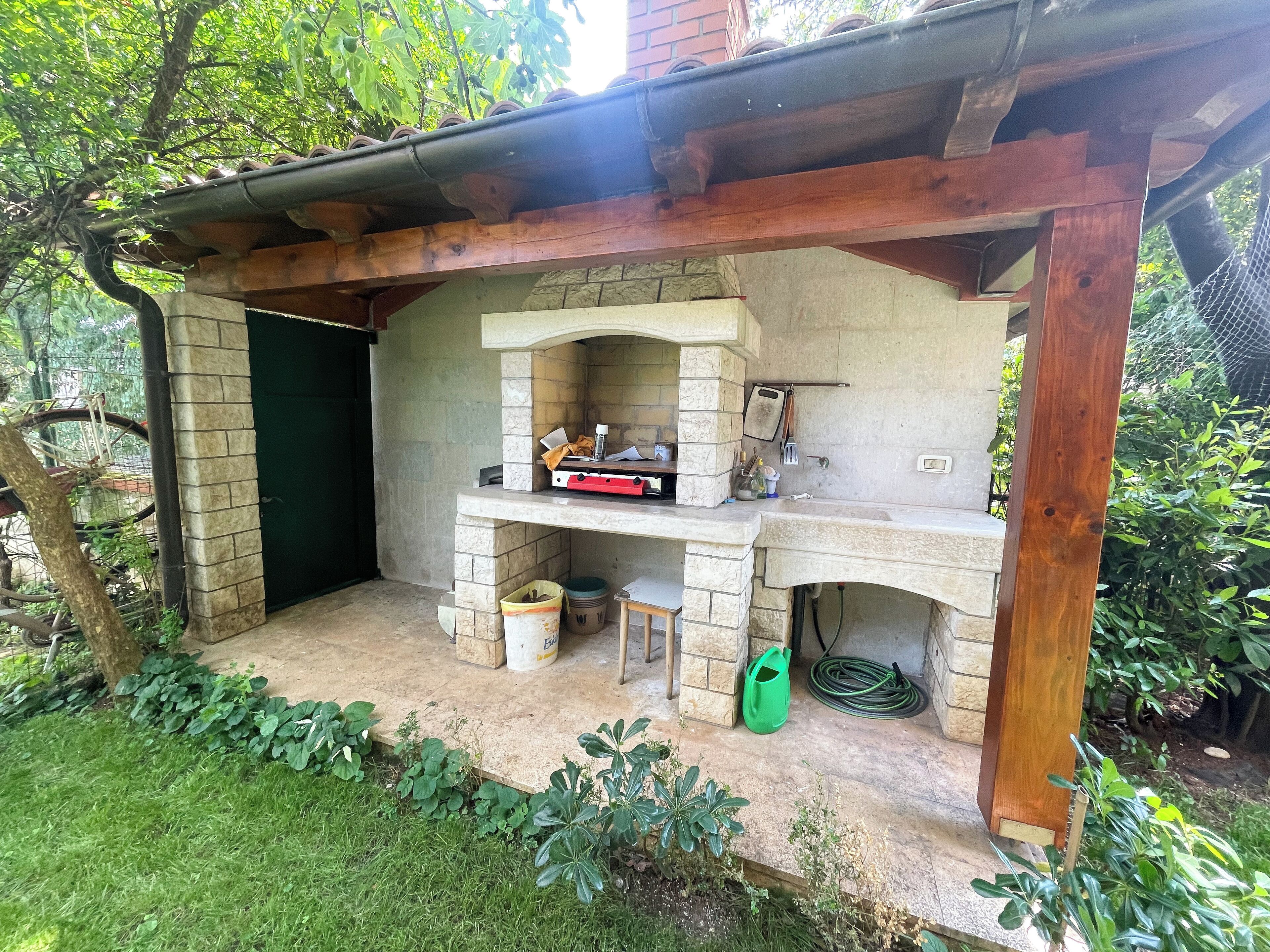 Una zona de cocina al aire libre con encimera de piedra, pérgola de madera y pared de ladrillo.