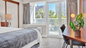 A hotel room with a bed, a desk, and a view of palm trees and buildings.