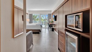 A modern hotel room with a bed, a desk, a microwave, and a refrigerator.