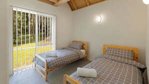 A bedroom with two wooden beds, a large window with blinds, and a view of a garden.