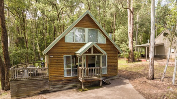 A wooden cabin with a porch, a deck, and a concrete pathway leading to the entrance.