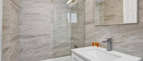 A modern bathroom with a glass-enclosed shower, a white sink, and a large mirror.