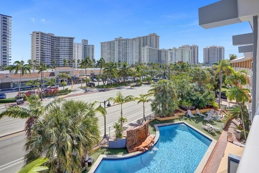 Un hôtel doté d’une piscine, de palmiers et offrant une vue sur les immeubles environnants.