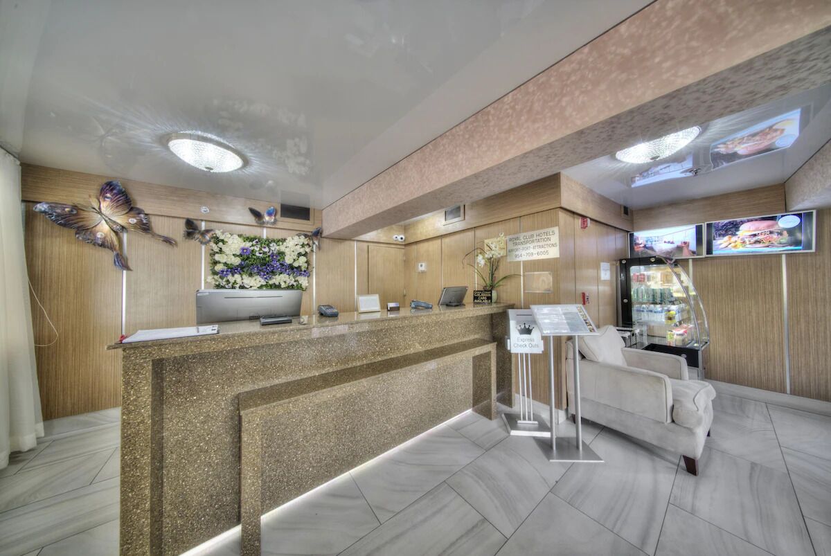 A hotel reception area with a granite counter, a floral wall decoration, a sofa, and a television screen displaying images.