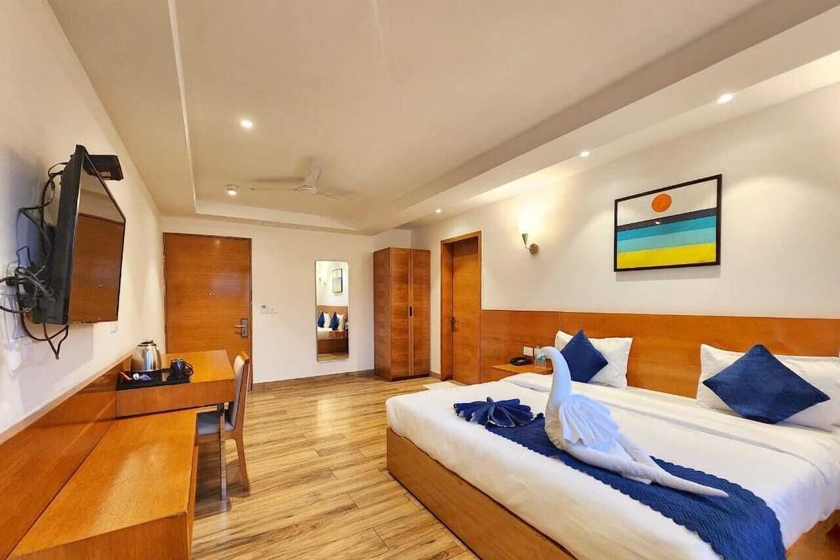 A hotel room with a bed, bedside table, desk, chair, and a television.