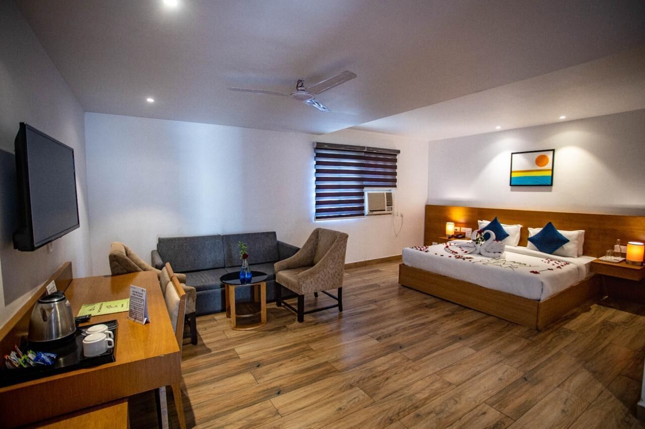 Habitación de hotel con cama, sofá, escritorio con cafetera, silla y televisor en la pared.