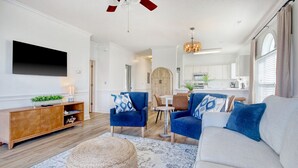 A modern living room with a flat-screen TV, blue armchairs, a grey sofa, and a wooden cabinet.