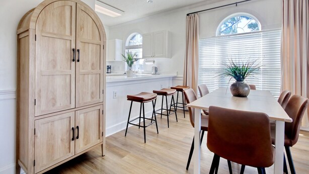 A modern kitchen with white cabinets, a wooden archway, and a dining area with a table and chairs.