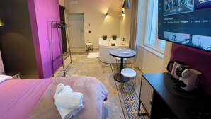 Een hotelkamer met een bed, een ronde tafel, een badkuip en een televisietoestel dat een programma vertoont.