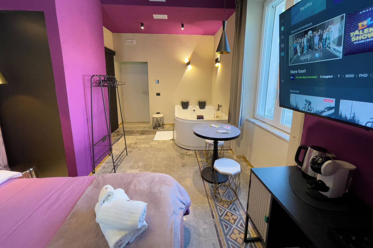A hotel room with a bed, a round table, a bathtub, and a TV displaying a show.
