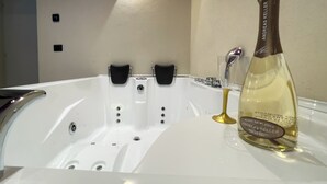 Een wit bad met twee zwarte handgrepen, een fles champagne en een glas op een witte aanrecht.