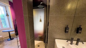 Een moderne badkamer met een grote witte wastafel, twee zwarte zeepdispensers en een douchehoek.