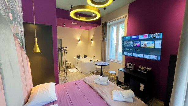 Een moderne hotelkamer met een bed, een badkuip, een kaptafel en een televisie waarop een streamingdienst wordt weergegeven.