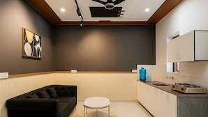 A modern kitchen with a black sofa, a round coffee table, and a ceiling fan. - Let'stay- Noida (Noida)