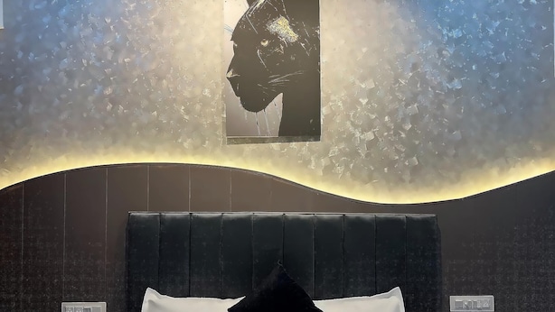 A bedroom with a bed, a headboard, a wall-mounted light fixture, and a power outlet. - Let'stay- Noida (Noida)