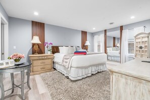 A bedroom with a bed, bedside tables, a dresser, a mirror, and a small table with a vase of flowers. - Barnstable Cape Cod Retreat | Pool, Fire Pit & BeachSticker (Barnstable)