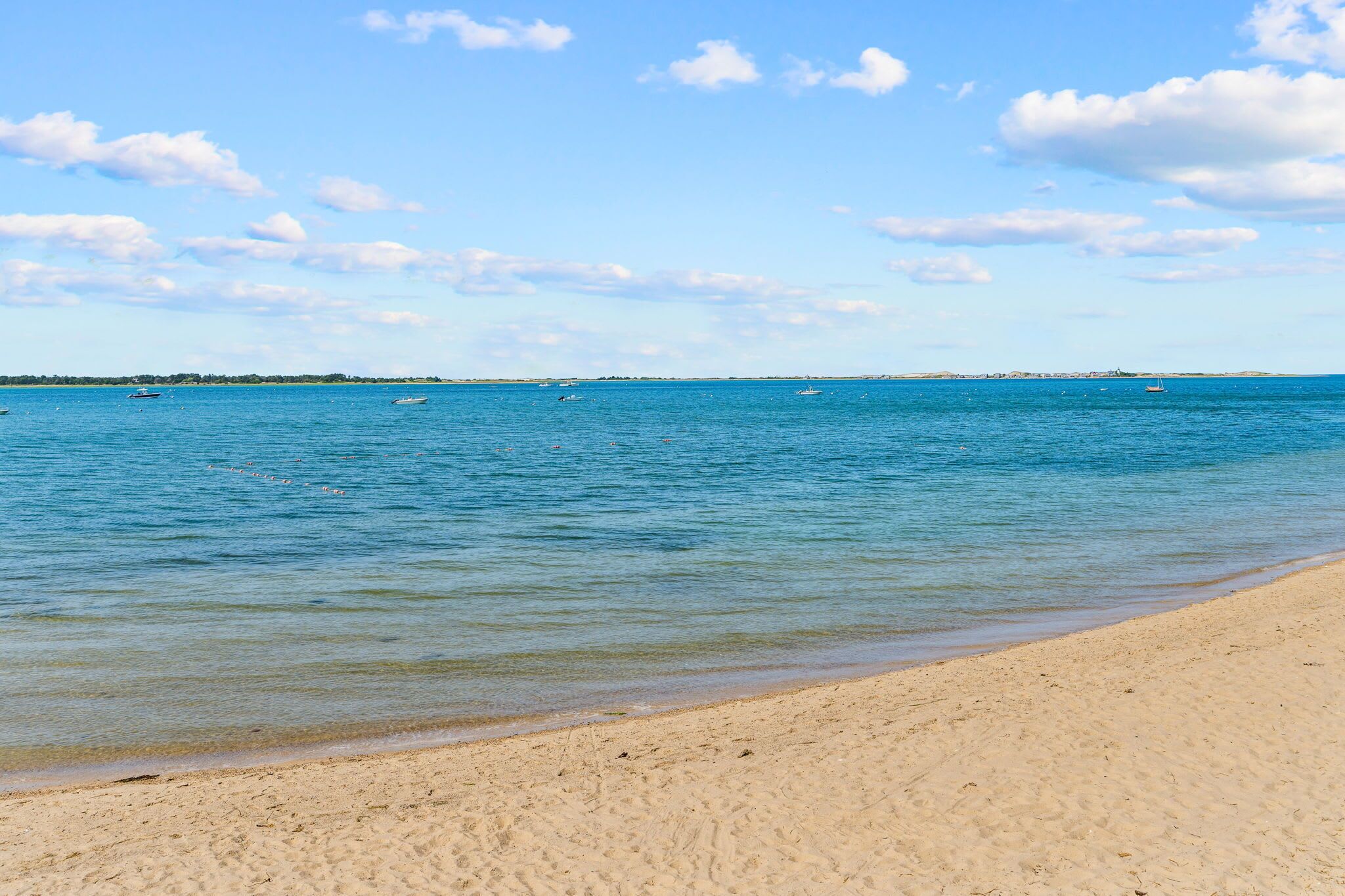 Een strand met helderblauw water, een zandstrand en boten in de verte.