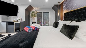 A modern hotel room with a large bed, a flat-screen TV, a desk with a computer, and a large window with a view of the outdoors. - Barnstable Cape Cod Retreat | Pool, Fire Pit & BeachSticker (Barnstable)