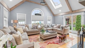 A spacious living room with high ceilings, a large window, and a cozy seating area. - Barnstable Cape Cod Retreat | Pool, Fire Pit & BeachSticker (Barnstable)