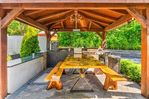 An outdoor patio with a wooden table and benches, a grill, and a sign reading "CAPESTOD". - Barnstable Cape Cod Retreat | Pool, Fire Pit & BeachSticker (Barnstable)