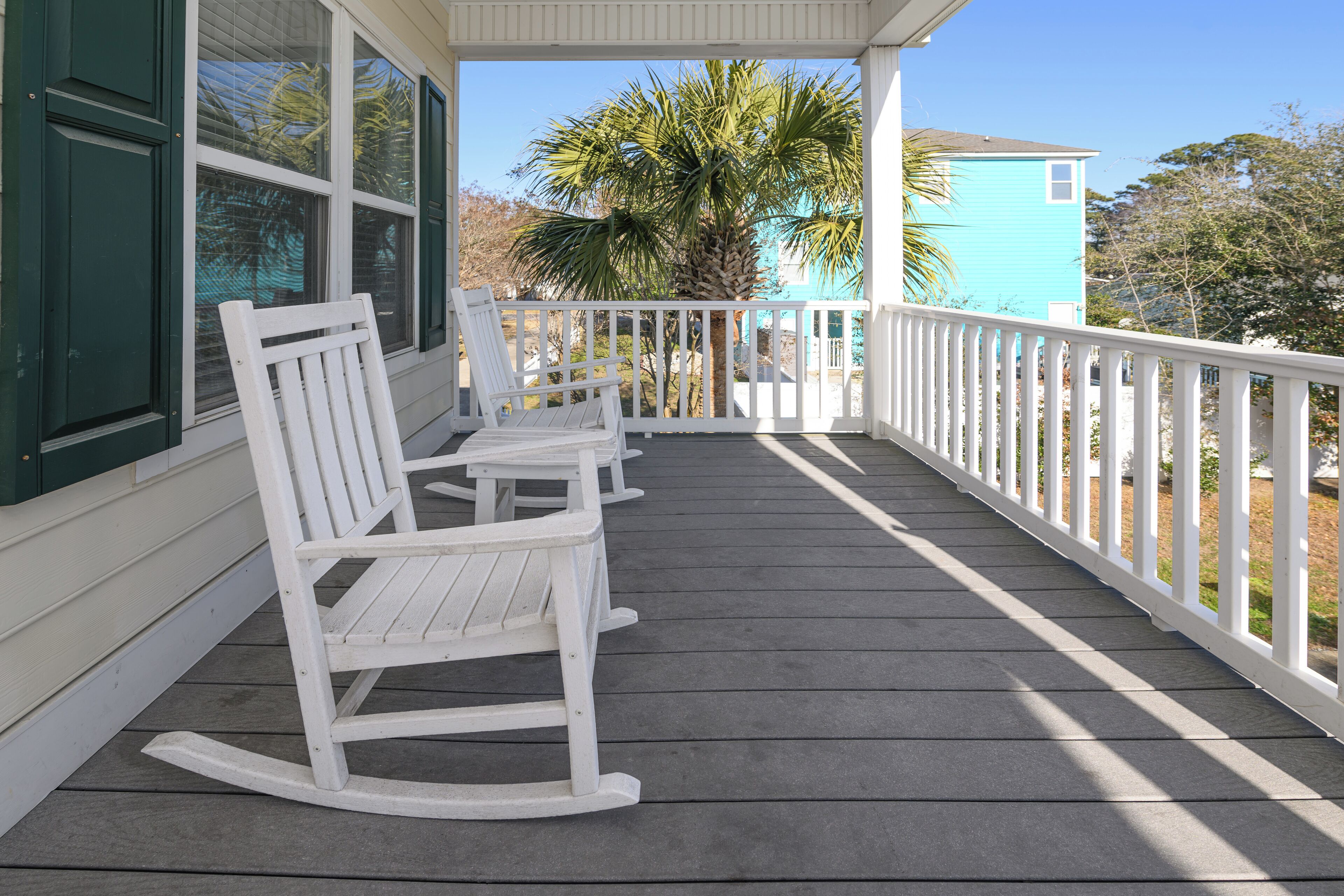 A wooden porch with white rocking chairs and a white railing.
