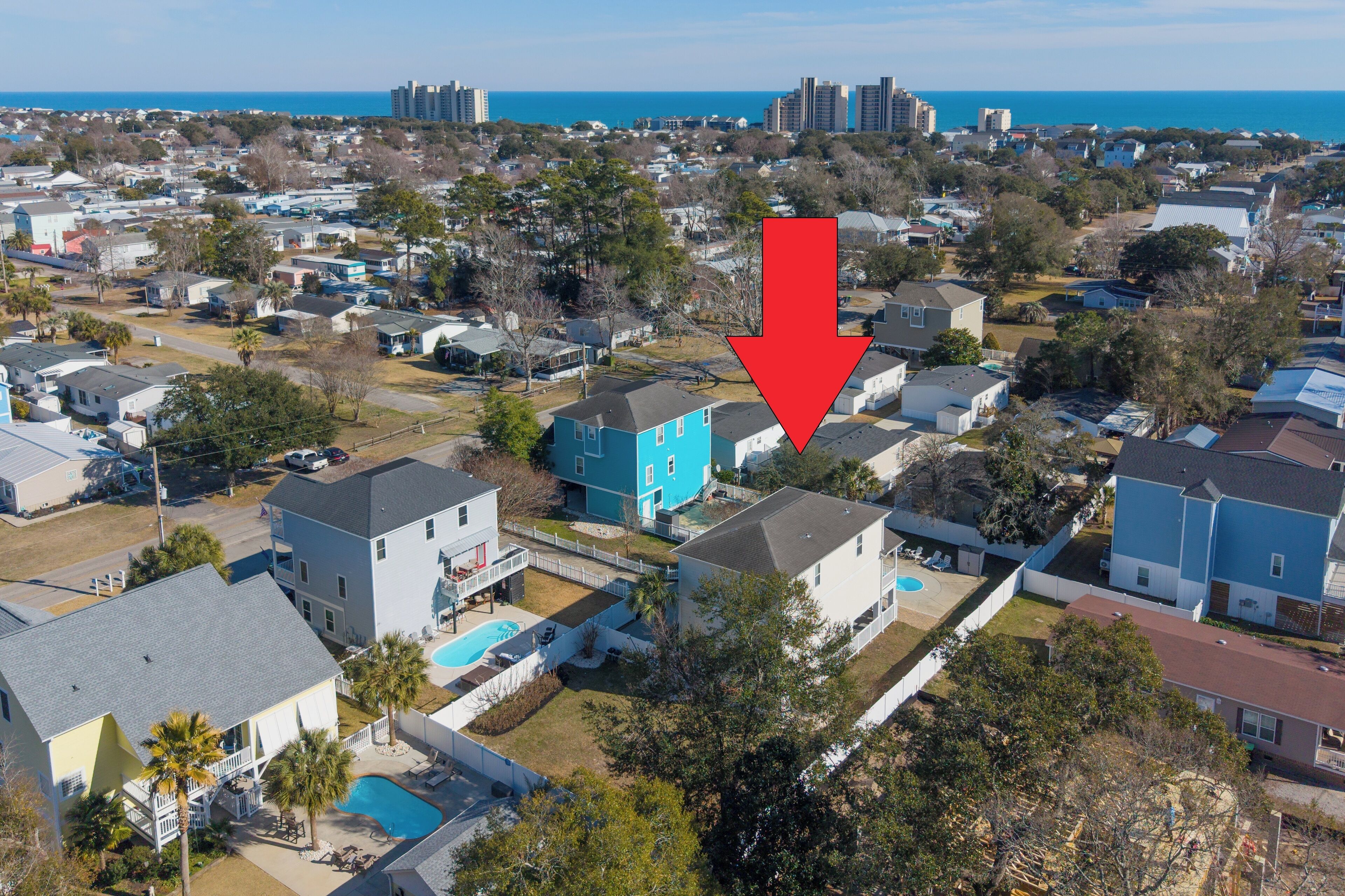 Vista aérea de una zona residencial con casas, una piscina y una gran masa de agua al fondo.