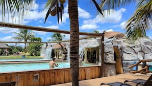 A pool area with a wooden deck, palm trees, and a stone wall.