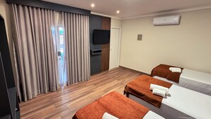 A hotel room with a wooden floor, two beds, a TV, and a window with curtains.