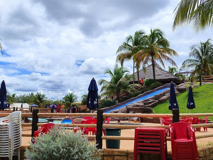 Area piscina di un resort con sedie di plastica rossa, ombrelloni e una struttura con tetto di paglia.