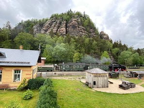 A train station with a steam locomotive, a small wooden building, and a grassy area with trees.
