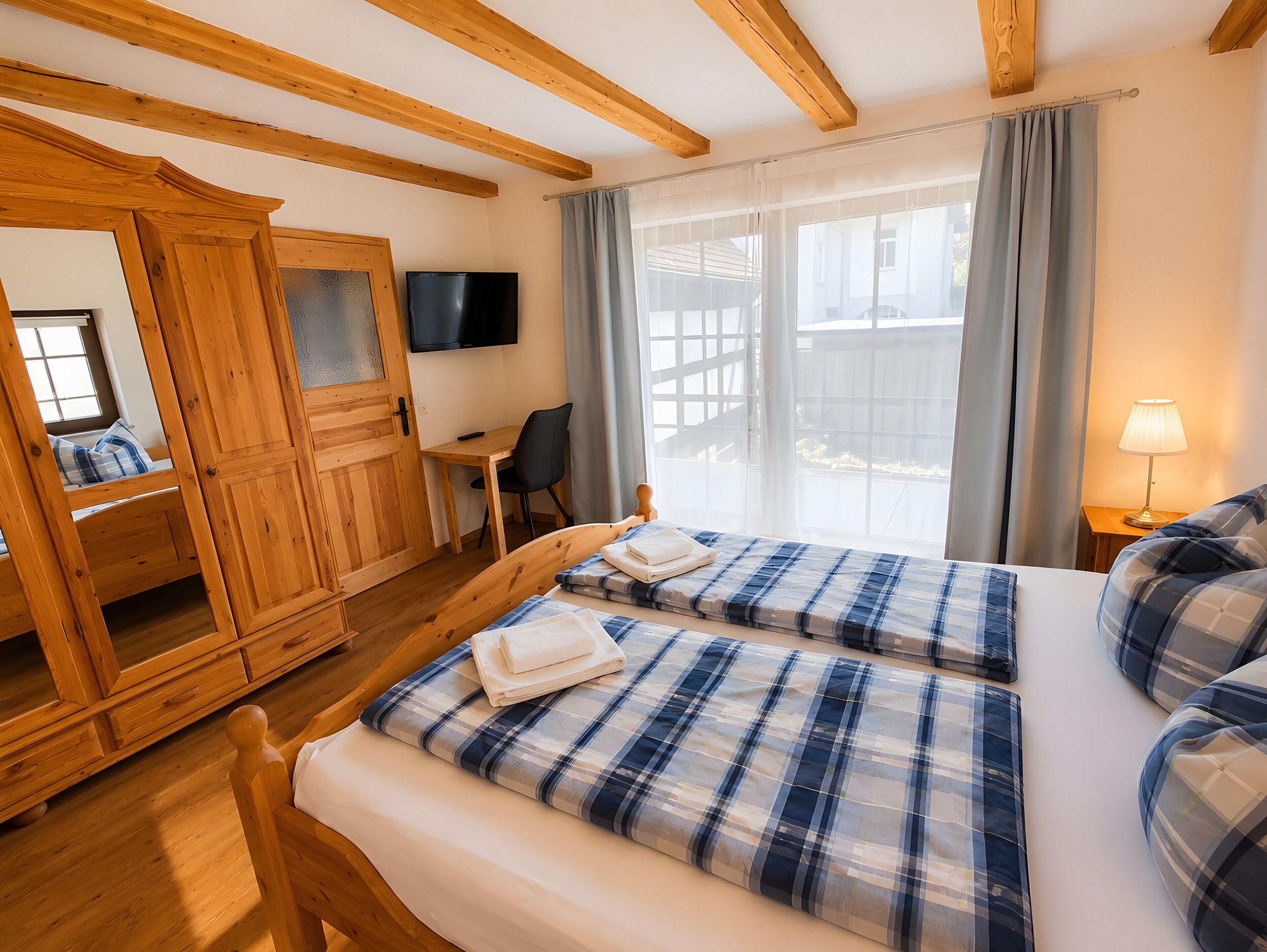 A room with a bed, a desk, a chair, a television, and a window with curtains.