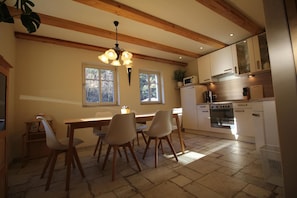 A dining area with a wooden table and chairs, a chandelier, and a kitchen with white cabinets and appliances. - Oberlausitzer Feha Mountain Cottage (Kurort Oybin)
