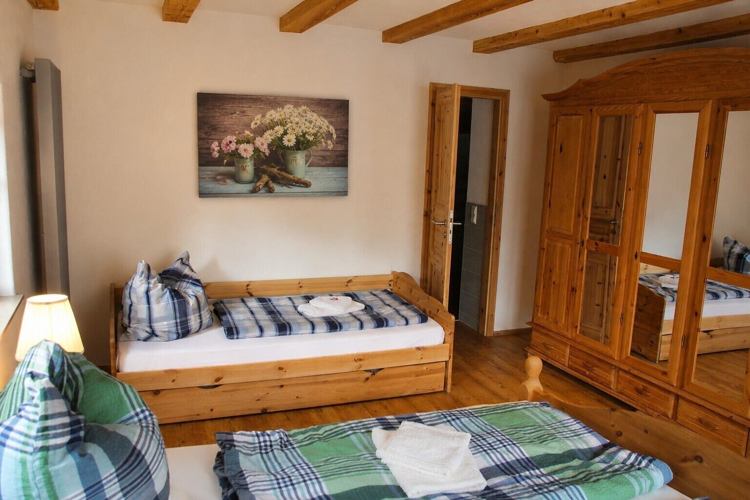 Un letto di legno con una coperta a quadri, un armadio in legno e un quadro con dei fiori appeso al muro.