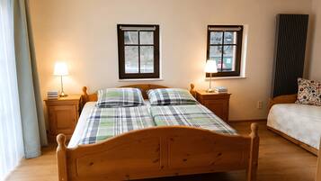A wooden bed in a room with two windows, a bedside table with a lamp, and a radiator.