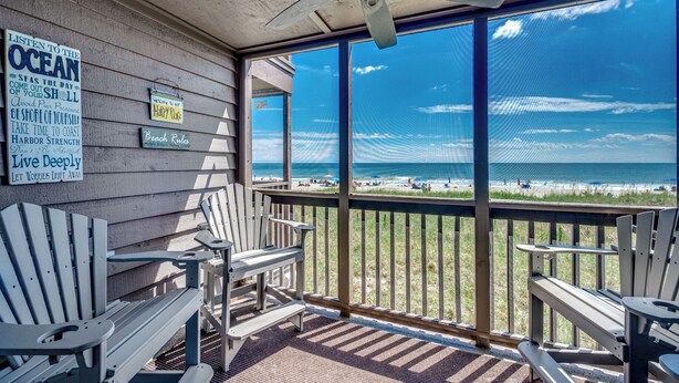 A covered deck with Adirondack chairs and a view of the beach. - ⛱️Oceanfront | Two Screened Balconies | 1st Floor Unit | Tilghman Beach 127🌊 (North Myrtle Beach)